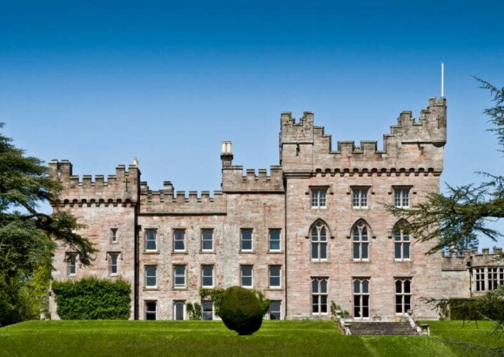 un gran edificio parecido a un castillo situado en lo alto de un exuberante campo verde